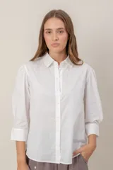 Camisa blanca de corte clásico con cuello camisero, cierre frontal de botones y mangas 3/4 con ligero fruncido en los hombros.