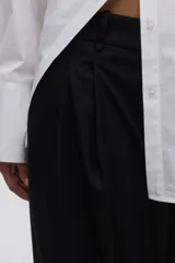 Pantalón sastrero negro de corte holgado con tiro alto, cierre con corchete y botón ocultos. Presenta piernas amplias con pinzas, raya marcada en el frente y la espalda, bolsillos al bies y bolsillos decorativos en la parte trasera.