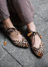 Ballerinas planas con diseño de rejilla y estampado animal print, con detalles de tiras cruzadas y borlas en el empeine.