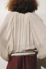 Blusa color beige confeccionada en viscosa, con cuello redondo y escote pico. Tiene mangas largas con puños y detalle de bordados con aplicación de abalorios en cuello, puños y ruedo. Diseño cruzado con fajín.