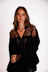 Camisa negra de manga larga con detalles de encaje en hombros y puños. Presenta un cuello tipo solapa y cierre frontal con botones dorados.