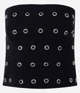 Blusa negra sin breteles, ajustada al cuerpo, con ojales metálicos distribuidos en la parte delantera y cierre de cremallera en la espalda. Confeccionada en bengalina con viscosa certificada.