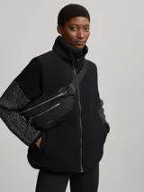 Chaleco negro capitoneado con cuello de piel sintética y cierre frontal con cremallera. Diseño sin mangas y corte recto.