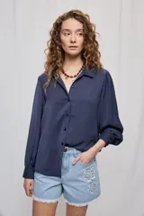 Camisa de manga larga color beige con cuello clásico y botonadura frontal. Presenta mangas con volumen sutil, puños abotonados y una silueta amplia de caída fluida.
