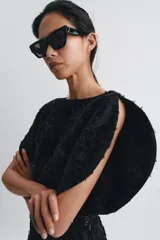 Vestido corto de cuello barco y manga corta abullonada, confeccionado en tejido negro con bordados florales y aplicaciones de abalorios y brillos a tono. Presenta un diseño con volumen en las mangas y cierre de cremallera oculta en la espalda.