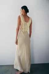 Vestido largo color beige de viscosa, con escote cuadrado, tirantes anchos, detalles drapeados, volantes y aplicaciones de encaje a contraste en el pecho. Cuenta con cierre trasero de botones.