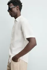Camisa de lino color beige de corte relajado, con cuello solapa, manga corta y cierre frontal con botones.