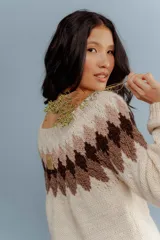 Buzo tejido a mano en lana merino, con diseño de patrón geométrico en forma de rombos en la parte superior en tonos marrones sobre base color crema.