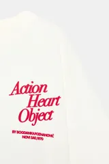 Camiseta de algodón color blanco hueso, corte regular, con cuello redondo y manga corta. Presenta un estampado pequeño en color rojo oscuro en el pecho con el texto "Action Heart Object" y detalles adicionales.
