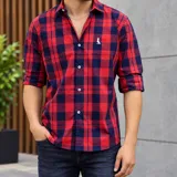 Camisa de manga larga con estampa de cuadros en tonos rojo y azul marino, con cuello clásico, cierre frontal de botones y bordado pequeño en el pecho.