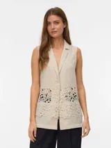 Top sin mangas color avena (oatmeal) con cuello en V y solapas tipo blazer. Presenta un panel central de encaje floral calado que deja ver la piel o la prenda interior.