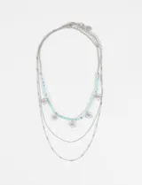 Collar triple de estilo delicado, compuesto por una cadena con cuentas celestes y dijes de flores plateadas, junto a dos cadenas simples de eslabones plateados.