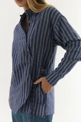 Camisa azul con rayas verticales grises, de algodón, cruzada, con cuello mao, mangas largas y cordón ajustable en la cintura.