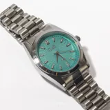 Reloj de pulsera plateado con esfera color turquesa y correa de eslabones metálicos.