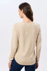Buzo tejido liso de manga larga con cuello redondo, confeccionado en algodón de tejido grueso. Presenta bordes acanalados en el cuello, los puños y la cintura, con un pequeño detalle de placa metálica en el lateral inferior.