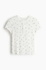 Top de manga corta en punto pointelle blanco con estampado floral diminuto en tonos rosados. Presenta cuello redondo con tapeta de botones.