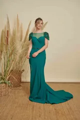 Vestido largo de fiesta color verde esmeralda, con escote ilusión, mangas cortas con detalles de pedrería y bordados, y cintura marcada con aplique de pedrería. Presenta una falda con caída fluida y pequeña cola.