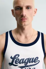 Camiseta sin mangas slim fit color blanco, con cuello redondo y sisas ribeteadas en azul marino. Estampado frontal con la palabra "League" y el número "'86" en azul marino.