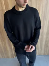 Sweater de hilo negro con cuello redondo, diseño de punto grueso y corte holgado. Presenta puños y ruedo acanalados.