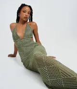 Vestido largo de punto color verde oliva, con escote pronunciado en V y espalda descubierta con tiras ajustables en el cuello y la espalda. Presenta un patrón geométrico de rombos y líneas en todo el tejido.
