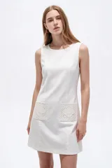 Vestido corto blanco de viscosa, sin mangas, con cuello redondo a la base y bolsillos frontales con apliques bordados.