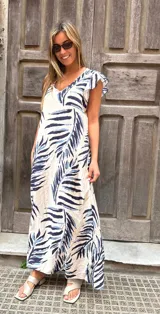 Vestido largo de corte holgado y fluido, con estampado de hojas tropicales en tonos azul marino y celeste sobre base cruda. Cuenta con escote en V y mangas cortas tipo volante.