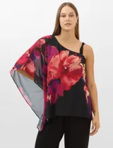 Enterito de seda fría con pantalón corte palazzo de pierna ancha. Presenta un diseño de un hombro descubierto con tirante fino y una sobrecapa asimétrica de gasa estampada con motivos florales en tonos rojos y fucsia sobre fondo negro que cae desde el hombro derecho.