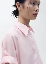 Camisa de manga corta color rosado, de diseño recto con cuello camisero y cierre frontal de botones.