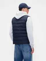 Chaleco puffer acolchado de color beige, con cierre frontal de cremallera, cuello alto y logo de la marca bordado en el pecho.