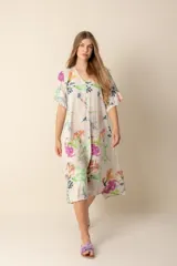 Vestido largo estampado con flores en tonos violeta, naranja, verde y azul sobre un fondo beige claro. Tiene cuello en V y mangas cortas.