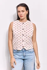 Top chaleco color arena con estampado de lunares marrones, confeccionado en tusor de algodón. Tiene corte entallado, sin mangas y cierre frontal con botones al tono.