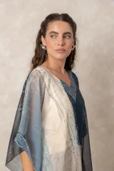 Blusa tipo túnica de gasa semitransparente con escote en V y mangas amplias. Presenta un diseño estampado con efecto acuarela en tonos azules, grises y marrones sobre fondo blanco.