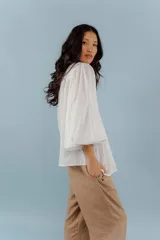Camisa de algodón color beige con cuello mao, cierre frontal con botones y mangas abullonadas con frunces en los hombros. Presenta costuras verticales decorativas en el frente.