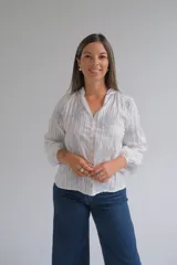 Blusa blanca de manga larga con diseño de rayas verticales y bordados florales en tono grisáceo. Presenta cuello camisero, cierre frontal con botones y puños elásticos.