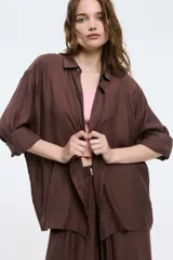 Camisa color marrón de corte oversized, con abotonadura frontal y en las mangas. Presenta un corte vertical en la espalda con lazos decorativos.