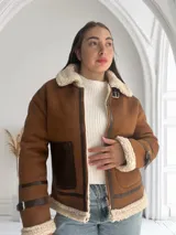 Chaqueta marrón con cuello de piel sintética color crema, cierre frontal con cremallera y hebilla en el cuello, bolsillos laterales con ribete de cuero marrón y puños con ribete de piel sintética.
