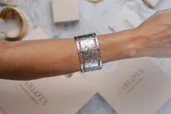 Pulsera tipo brazalete rígido de acero quirúrgico color plateado, con diseño de textura martillada y aberturas laterales geométricas.