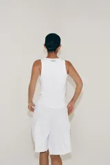 Top de algodón blanco con escote redondo, sin mangas y cierre frontal con pequeños botones. Presenta un diseño acanalado y bajo redondeado.