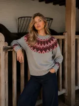 Buzo de lana merino con diseño nórdico en el canesú, cuello redondo y mangas largas. Presenta un patrón geométrico en tonos rosa y bordó sobre una base de color gris.