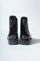 Botín Chelsea de mujer, color negro charol, con elástico lateral y punta cuadrada. Posee un taco bajo y plano.