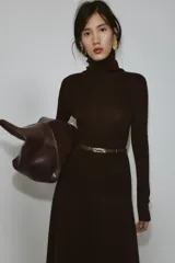 Jersey de punto liso confeccionado en 100% lana, con cuello subido y manga larga. Incluye un cinturón fino integrado en la cintura con hebilla metálica.