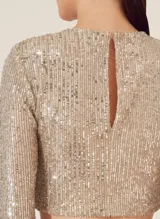 Blusa corta dorada cubierta de lentejuelas, de mangas largas y cuello redondo.