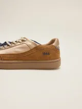 Championes urbanos de cuero en tonos tostado y marrón claro, con detalles en rojo, cordones bicolor, suela de goma y el número 1986 bordado en el talón.