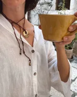 Collar artesanal con dije de flor en bronce o alpaca, suspendido en un cordón de seda natural teñido a mano. El diseño permite atarse con un moño, ofreciendo versatilidad para lucirlo de distintas formas.