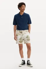 Bermuda de corte clásico con estampado tropical de palmeras y paisajes en tonos tierra sobre fondo beige. Cuenta con cierre de botón y cremallera, bolsillos laterales y bolsillos traseros.