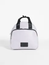 Mochila pequeña de cuero sintético color lila, con cierre frontal, bolsillo externo con cierre y manijas superiores de cinta negra. Incluye parche con logo en la parte inferior.