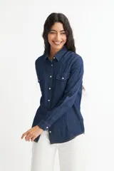 Camisa de denim azul con dos bolsillos frontales con botón, corte recto y mangas largas con puños abotonados.