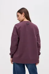 Buzo oversize de felpa con friza, color bordó, con cuello redondo, mangas largas con cortes decorativos y tajos laterales en el ruedo. Presenta un bordado de la marca en una de las mangas.