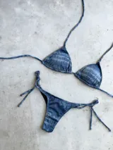 Bikini azul con efecto desgastado y brillo. El top es de triángulos movibles con almohadillas desmontables y se ata al cuello y espalda. El bottom es colaless y se ata a los costados.