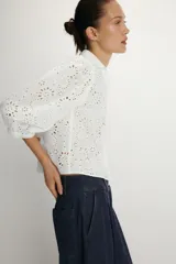Camisa de cuello solapa y escote en pico, confeccionada en tejido con bordados perforados a tono. Presenta mangas abullonadas por debajo del codo y cierre frontal con botones.